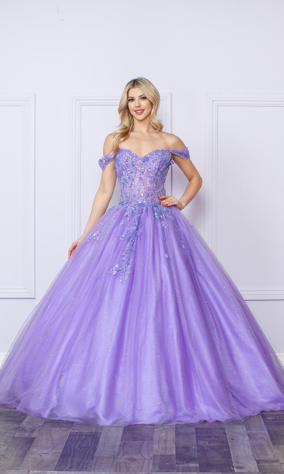 A woman in the Bright Off-the-Shoulder Long Prom Ball Gown H1349, a floor-length lavender dress with floral embellishments, stands against a light-colored wall.